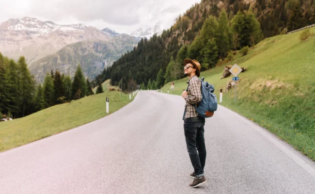 young-man-trendy-hat-standing-middle-highway-looking-away-enjoying-fresh-air-near-italian-alps